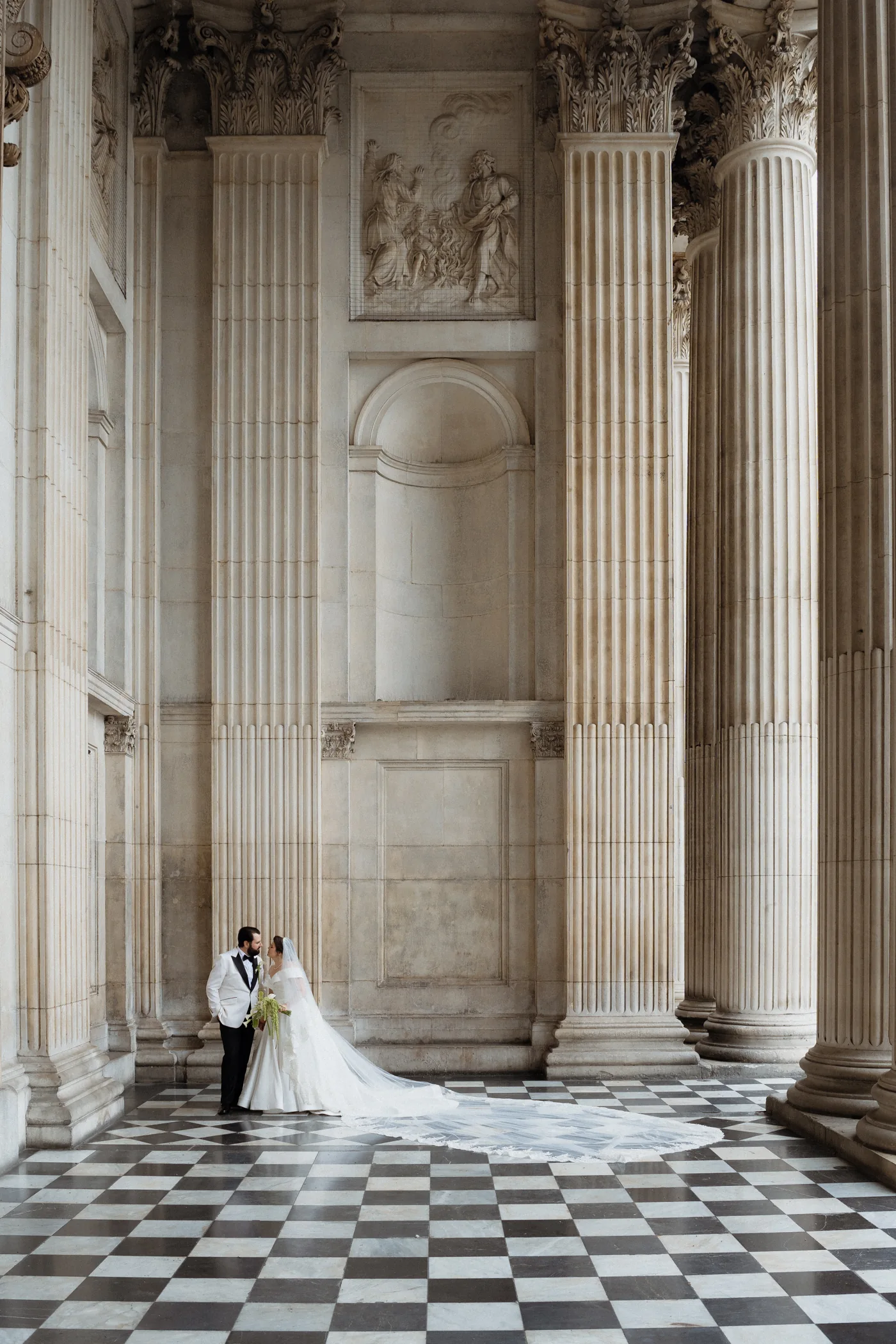 Couple beneath tall stone columns on a chequered floor