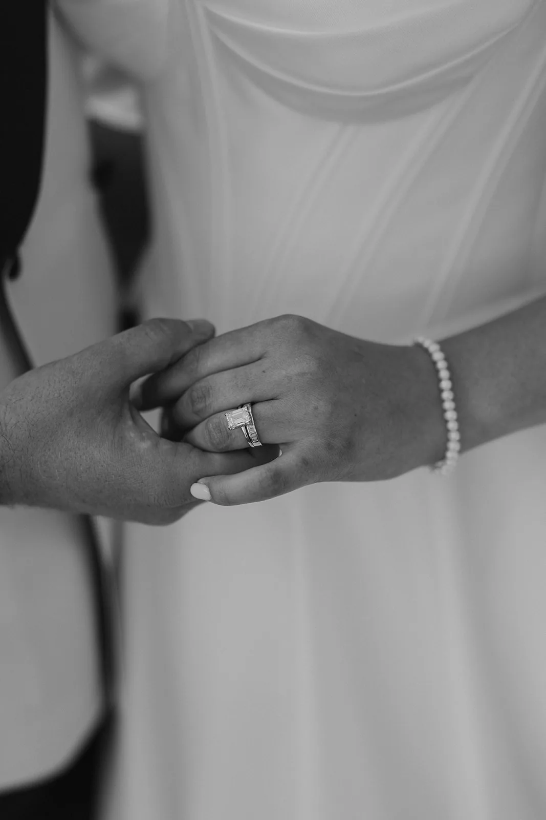Black-and-white close-up of bridal jewellery and clasped hands